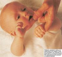 Ребенок зажимает палец, положенный в его ладонь